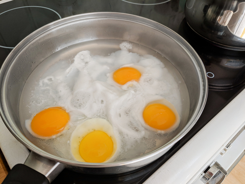 four eggs being poached in a pot of hot water